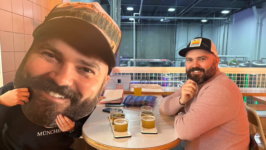 Man in a hat sitting next to a big head cutout of his face